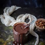 jar of homemade Nutella, cheesecloth, hazelnuts in a bowl