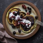 A plate with three pancakes topped with yogurt and berries. Fork leaning on the plate and a napkin on the side.