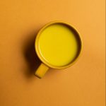 Yellow cup with a golden milk in it. On a yellow background.