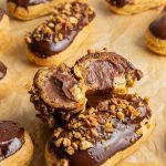 Chocolate eclairs on a parchment paper. One eclair cut in half showing the inside by leaning on another eclair.