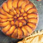 Plum upside-down cake with sliced fresh plums next to the cake and a yellow napkin.