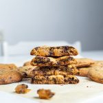 Ginger chocolate orange cookies in half one on top of each other. More cookies around them with broken bits in front of them. A chair on the background.
