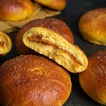 Half of a bun filled with jam leaning on top of other buns.