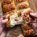 Two hands pulling bread roll stuffed with cheese.