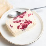 A plate with a slice of Sour Cherry Ice Cream and a spoon next to it.