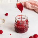 Jar with raspberry sauce and a spoon dripping over it.