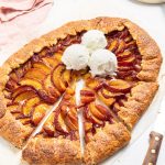 Peach galette with cut out slices and vanilla ice cream scoops on top.