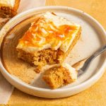 Pumpkin cream cheese bar on a plate with a fork and a pice of the cake on it.