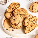 Butterscotch chocolate chip cookies stacked on a plate with some broken in half.